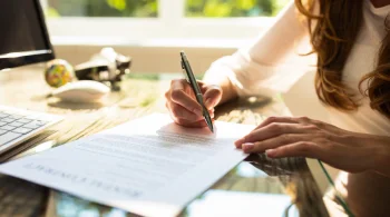 Close up of a woman's hands as she signs a legal document at her desk.