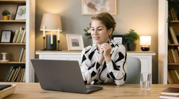 A woman sits in her home office and looks at her laptop.