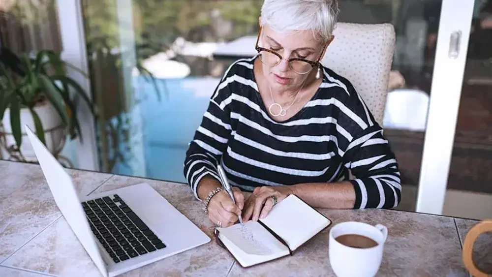 A woman sits at a kitchen counter and takes notes on living trusts. Assigning financial accounts to the trust constitutes another vital step in the process of transferring assets to a living trust.