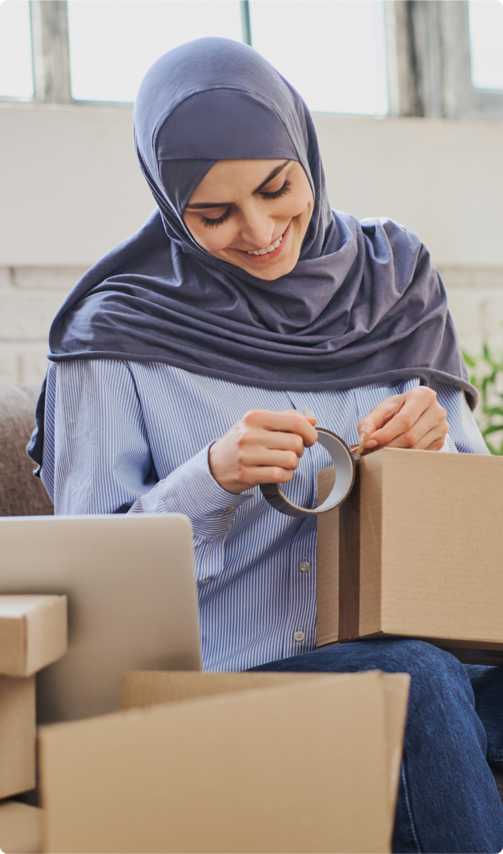 A woman wearing a hijab taping a box closed.
